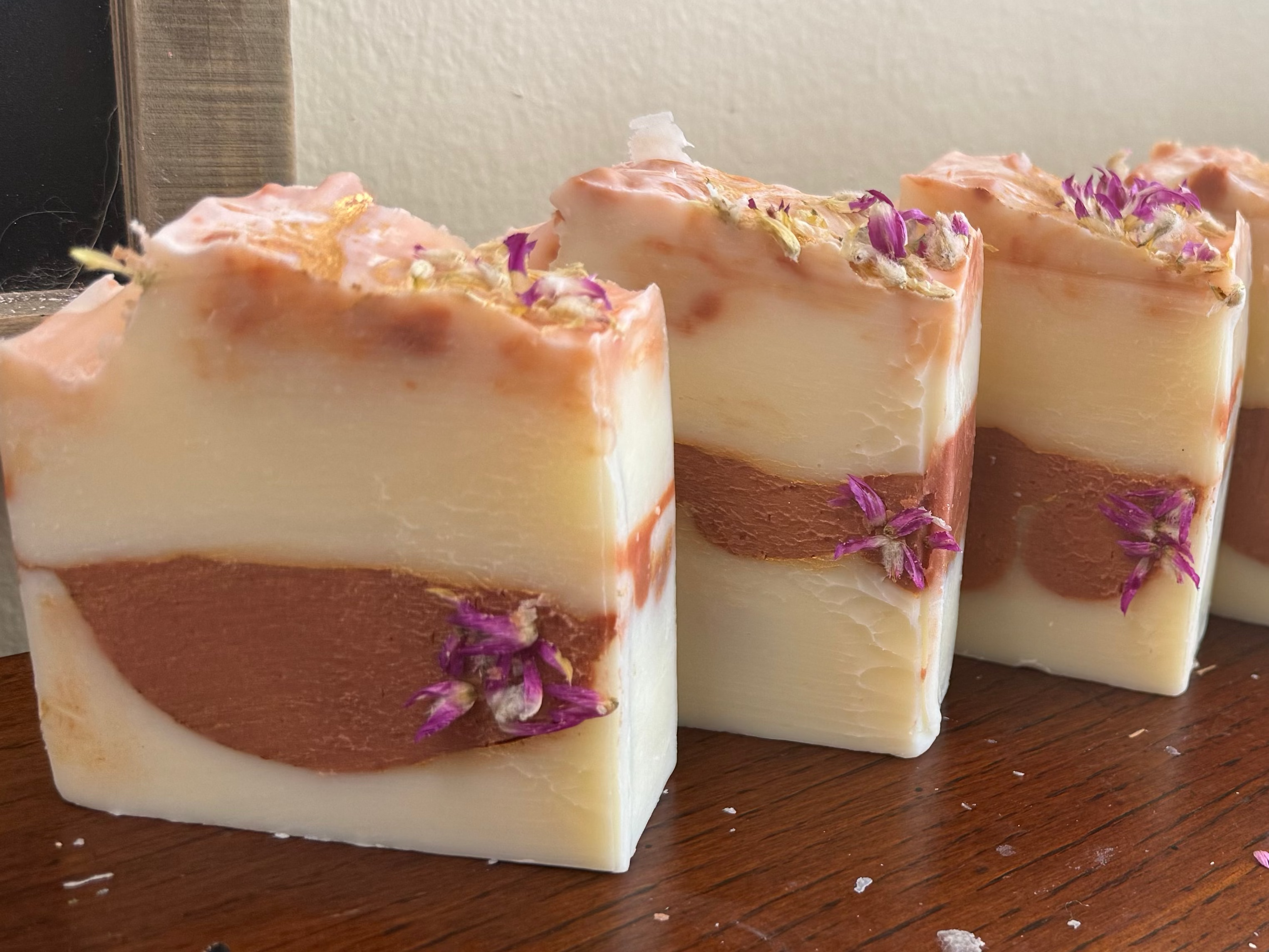 Row of layered soap bars with purple flowers on a wooden surface